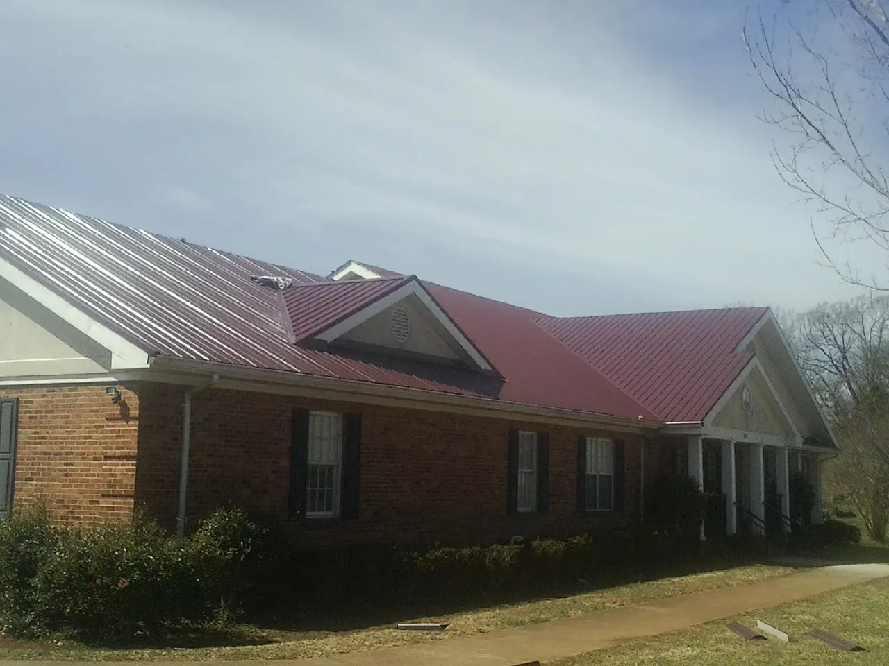 Red metal roof with gabled entries on a long brick building, from a Hail Damage Roof Repair job in Brigantine