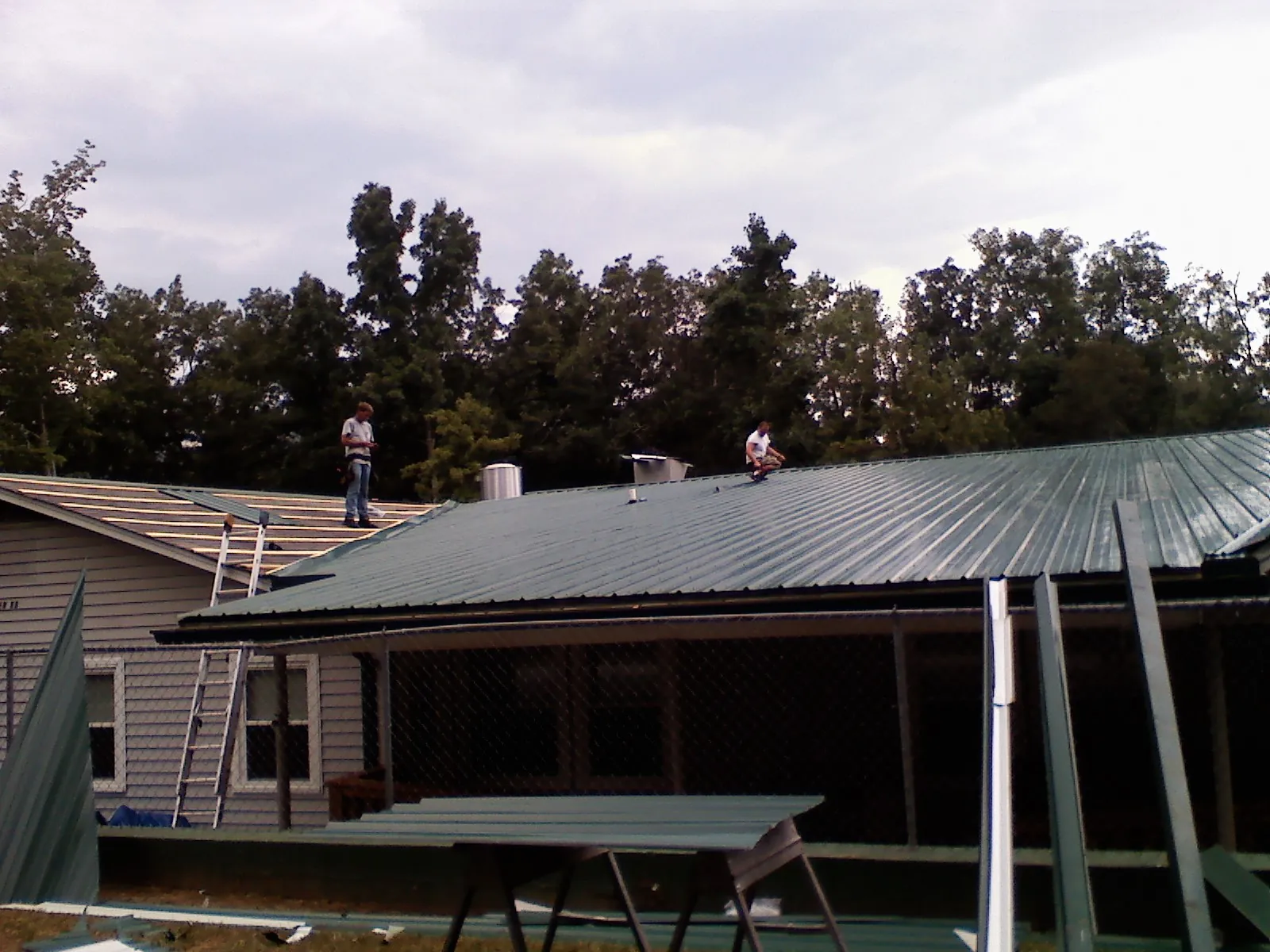 Two roofers installing green metal panels above a covered porch in Brigantine