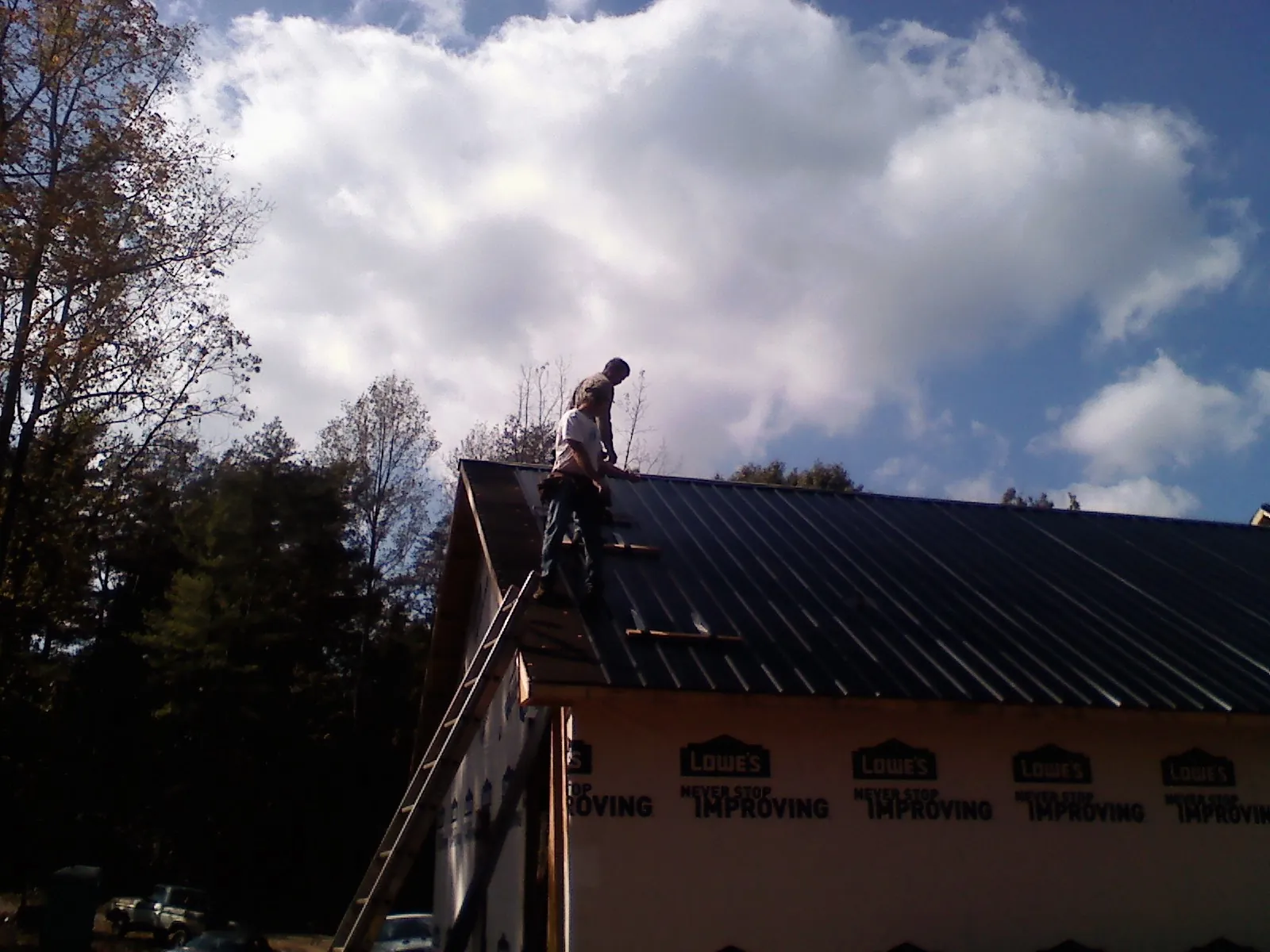 Roofer fastening dark metal panels high against a cloudy sky, from a Roof Inspection job in Brigantine